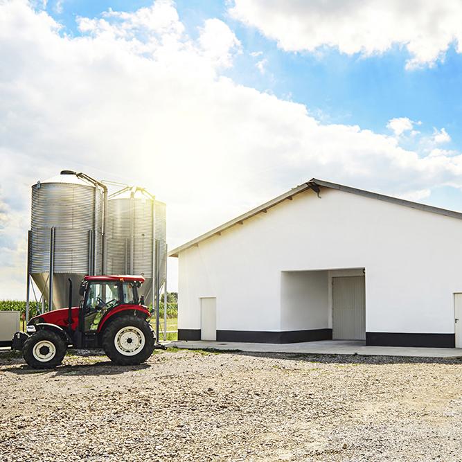 A poultry barn with a red tractor an silos outside of it